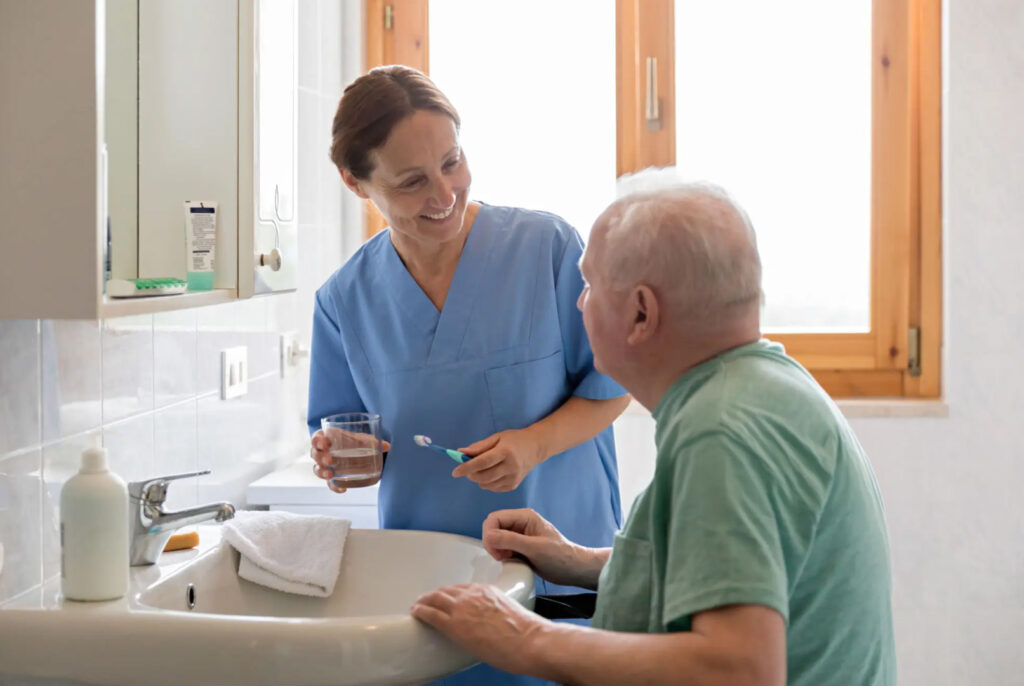 Eine Pflegefachkraft der private Spitex hilft einem älteren Mann im Badezimmer beim Zähneputzen – beide lächeln sich an. Die Szene vermittelt Fürsorge, Selbstbestimmung im Alter und persönliche Betreuung zu Hause. Dieses Bild veranschaulicht die Mission der IAHA (International Association for Healthy Aging), gesundes Altern durch individuelle Unterstützung im Alltag zu fördern.